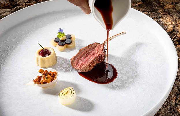 Fleischgericht mit einer Lammkeule und kleinen Beilagen auf einem weißen Teller